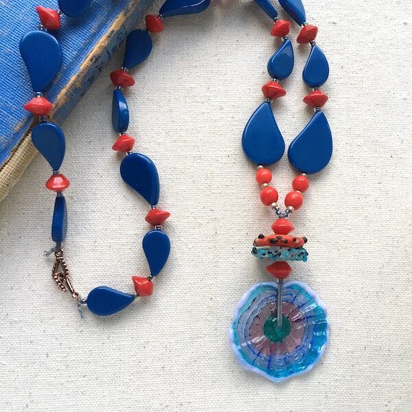 Blue paisley shaped beads with red accent beads and wavy donut glass pendant. 